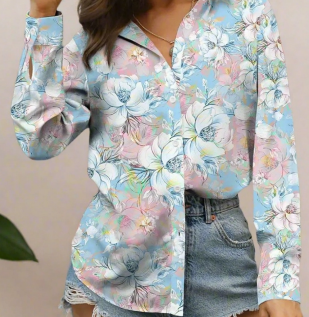 A woman dressed in a pastel-coloured blouse with large, soft floral prints in shades of blue and pink, worn with high-waisted denim shorts.