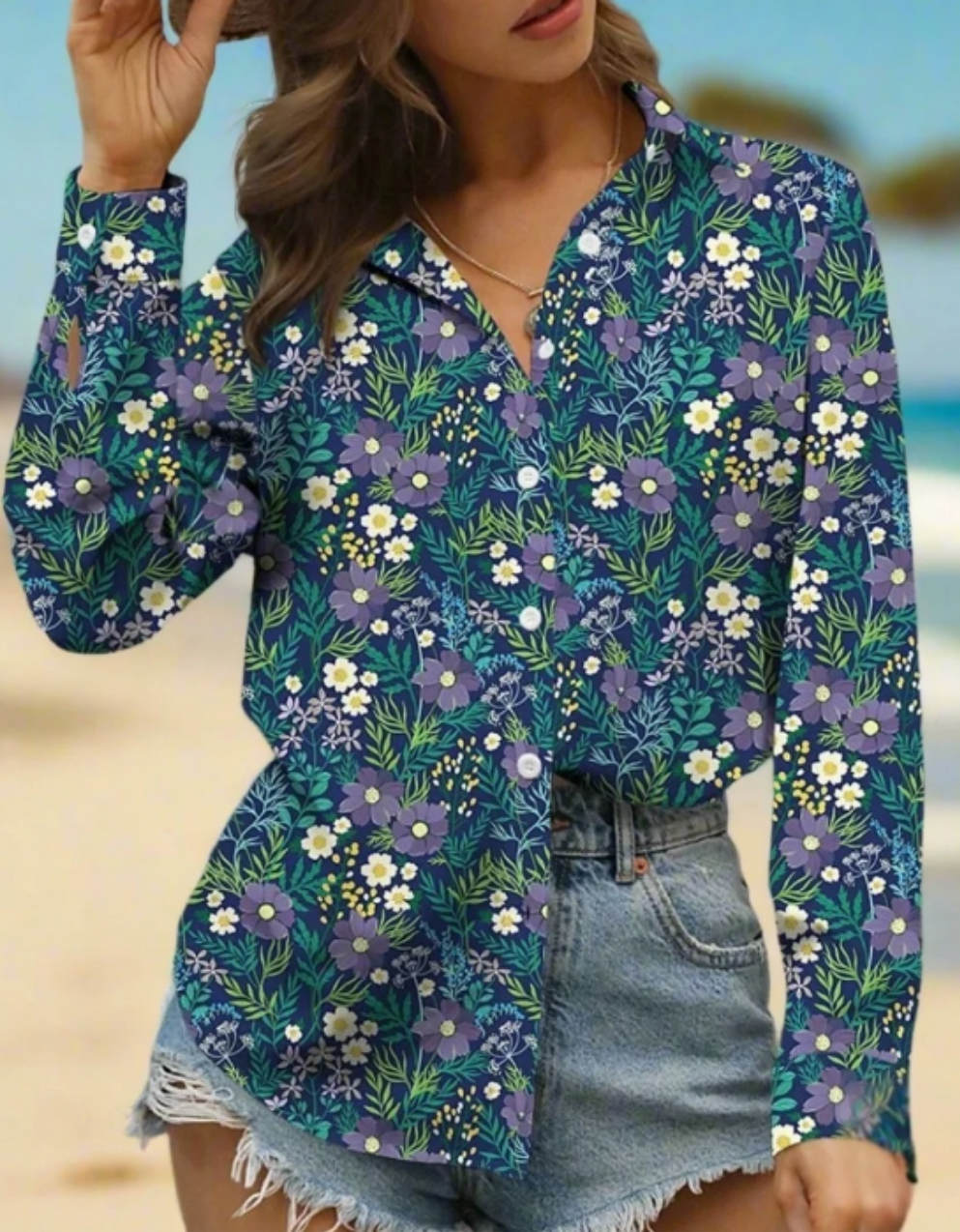 Woman wearing a long-sleeve floral button-up blouse with a turn-down collar, styled casually with denim shorts on a beach background