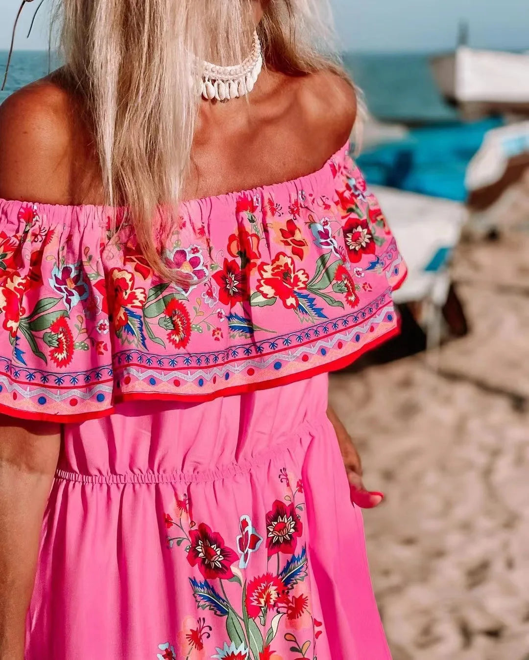 Close-up of woman in pink off-shoulder floral dress with ruffle trim and shell necklace on the beach