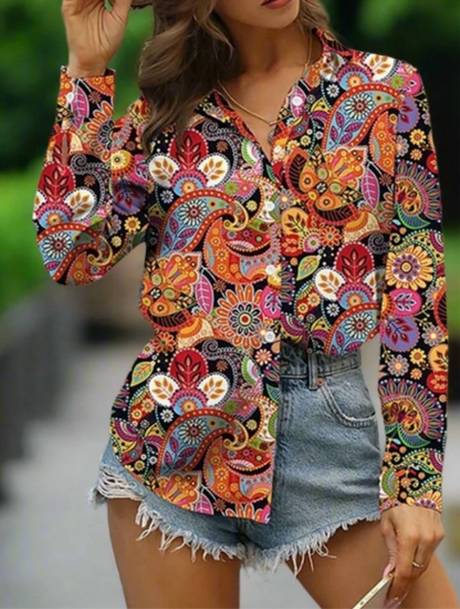 A woman wearing a vibrant, colourful floral-patterned blouse with long sleeves and a V-neck paired with denim shorts.