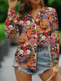 A woman wearing a vibrant, colourful floral-patterned blouse with long sleeves and a V-neck paired with denim shorts.