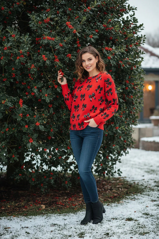 Woman wearing a vibrant red long-sleeve sweatshirt with a black bow print, standing outdoors in a garden with winter greenery.
