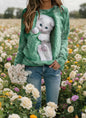 Lifestyle photo of woman in olive green cat-themed sweatshirt with 3D kitten design, standing in flower field