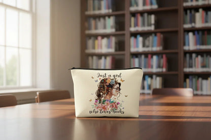 Pouch with a design of a girl with flowers and text 'Just a girl who loves books' on a table in a library setting.