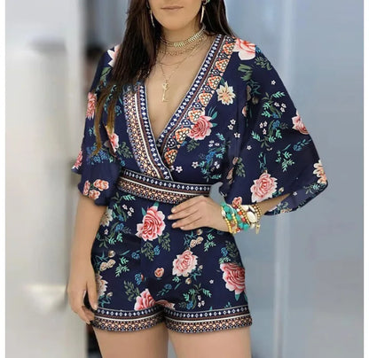  Woman wearing a navy floral romper with yellow and red roses, posing outdoors.