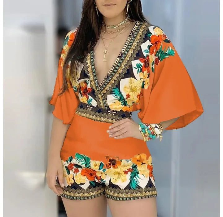  Woman in an orange floral romper with wide sleeves, standing on a beach.