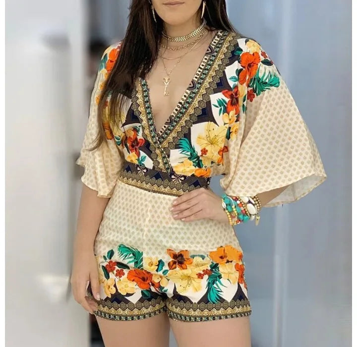 Woman wearing a cream romper with red and green floral patterns, accessorized with a belt