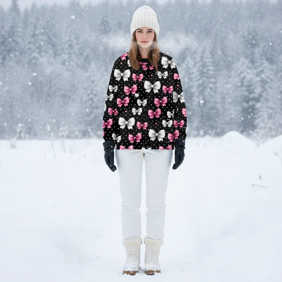 Black winter-ready sweatshirt with clusters of pink, white, and red bows, worn in a snowy forest landscape.
