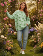 Pastel sage green bow-print sweatshirt in a lush, blooming garden environment.