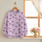 Purple bow-patterned pullover displayed near a window with floral accents.
