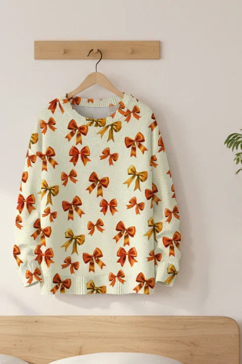 Warm cream sweater with orange bow patterns hanging on a natural wood hook.