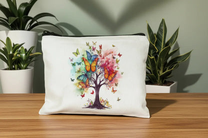 White pouch with a colourful tree and butterflies design on a wooden surface with plants in the background.