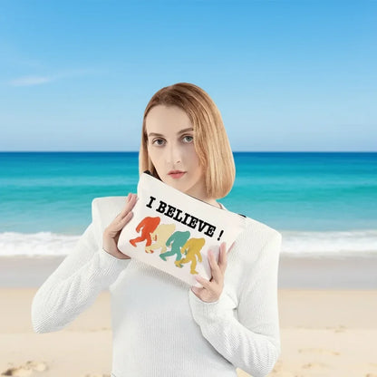 Woman holding a pillow with 'I Believe!' and colourful silhouette design in front of a decorative wall with makeup items.