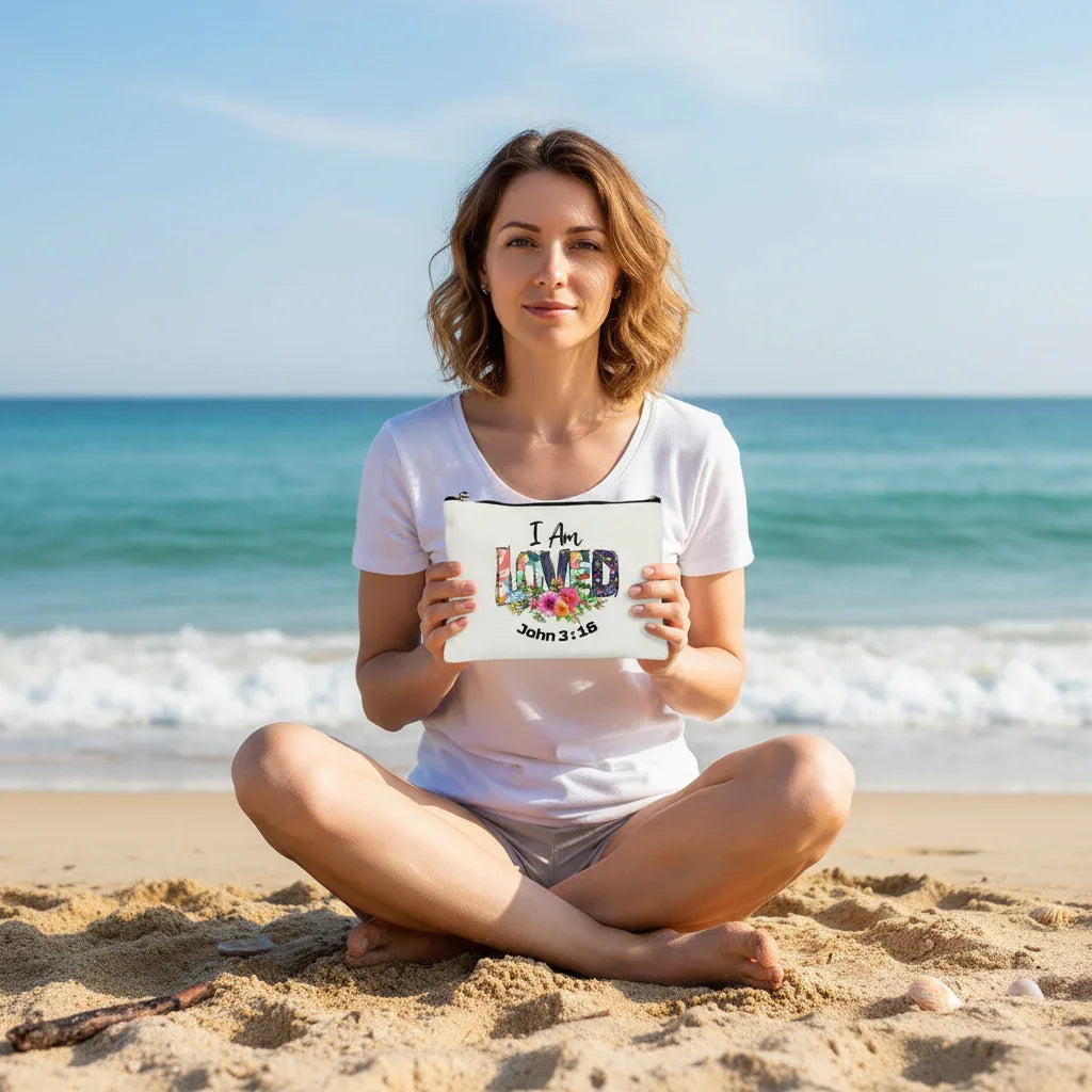 Woman sitting on a beach holding a sign that reads 'I Am LOVED John 3:16'.