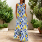 White sleeveless maxi dress with intricate blue floral and vine patterns, modelled indoors beside a potted plant