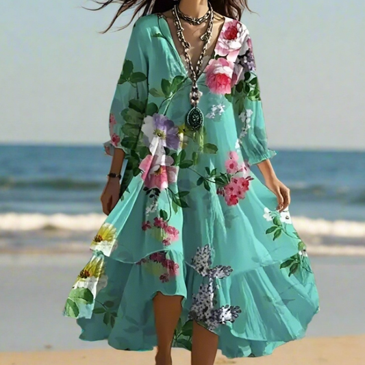 Woman wearing a teal floral print V-neck long sleeve dress with irregular lotus leaf hem, standing on the beach during sunset.