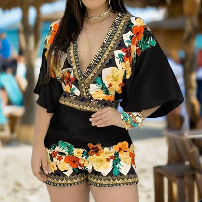 Woman wearing a black floral romper with yellow and red roses, posing outdoors