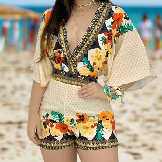 Woman wearing a cream-colored romper with multicoloured floral prints and geometric borders, standing on a beach