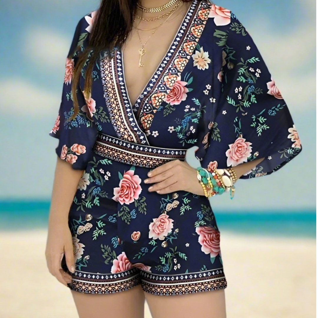 Woman wearing a navy blue romper with pink floral prints and intricate border patterns, standing on a beach