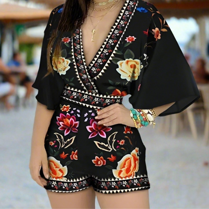 Woman wearing a black floral romper with yellow and red roses, posing outdoors