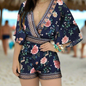 Woman dressed in a navy and floral romper with gold detailing in a tropical beach setting